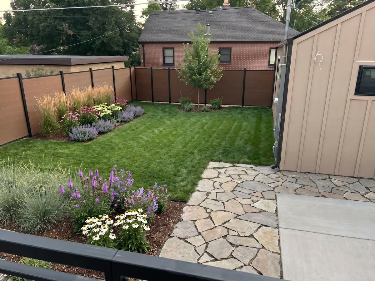 The same backyard replanted: new lawn, mulched beds of grasses, coneflowers, liatris, and catmint, a flagstone path, and a young tree